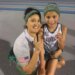 Emelie Chavez, the 7-year-old world record holder in the 3000M, and an adult pose for a picture on a track, both holding up one finger to signify their accomplishment.