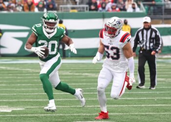 A New York Giants player, number 20, runs with the football while a New England Patriots player, number 53, pursues.