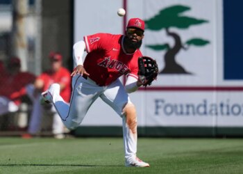 Jo Adell, wearing an Angels uniform, lunges to catch a baseball.