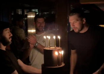 Luka Dončić blowing out birthday candles as Novak Djokovic claps behind him.