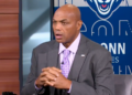 Charles Barkley speaking with his hands clasped together, wearing a gray suit and purple patterned tie.