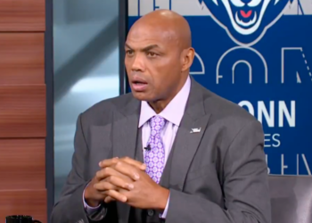 Charles Barkley speaking with his hands clasped together, wearing a gray suit and purple patterned tie.