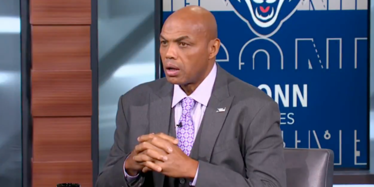 Charles Barkley speaking with his hands clasped together, wearing a gray suit and purple patterned tie.