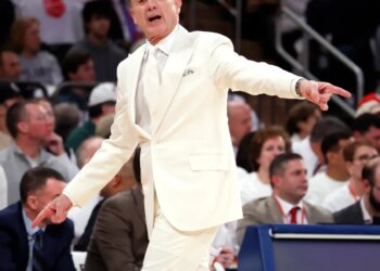 St. John's head coach Rick Pitino in a white suit, shouting and pointing during a game against Villanova.