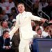 St. John's head coach Rick Pitino in a white suit, shouting and pointing during a game against Villanova.