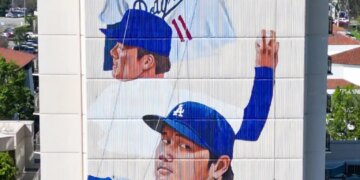 Mural of two Dodgers players on a building, with two workers on a platform painting below.