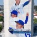 Mural of two Dodgers players on a building, with two workers on a platform painting below.
