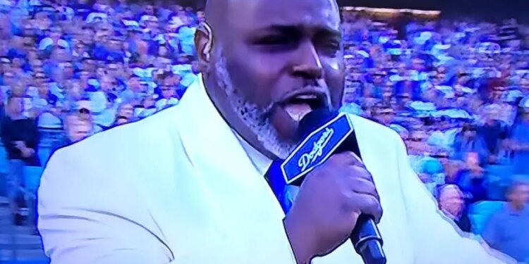 Gospel singer Keith Williams Jr. singing the national anthem with a microphone that has "Dodgers" written on it.