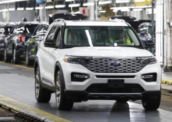 White Ford Explorer being driven in a factory with other SUVs in the background.