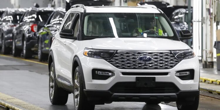 White Ford Explorer being driven in a factory with other SUVs in the background.