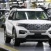 White Ford Explorer being driven in a factory with other SUVs in the background.