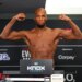Michael Page posing shirtless on a weigh-in scale, flexing his arms.