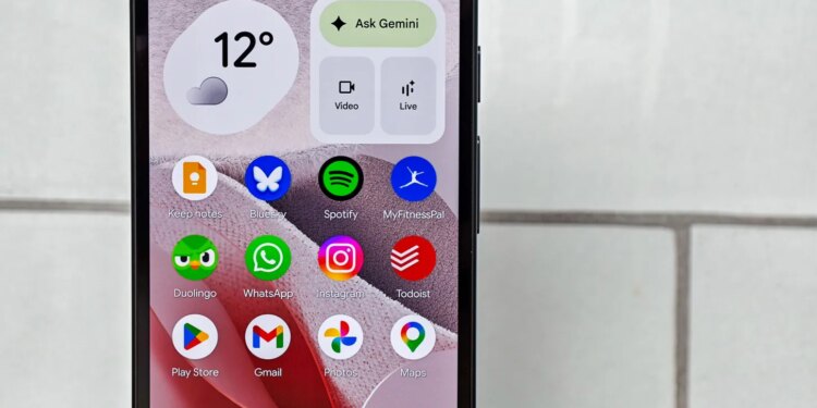Photo of Google Pixel 10A in front of white tiles, showing the home screen