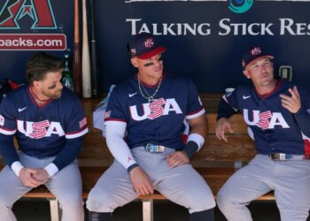 United States' Bryce Harper, left, Aaron Judge, center, and Alex Bregman sit in the team dugout prior to an exhibition baseball game against the Colorado Rockies Wednesday, March 4, 2026, in Scottsdale, Ariz.