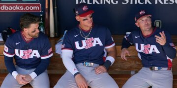 United States' Bryce Harper, left, Aaron Judge, center, and Alex Bregman sit in the team dugout prior to an exhibition baseball game against the Colorado Rockies Wednesday, March 4, 2026, in Scottsdale, Ariz.