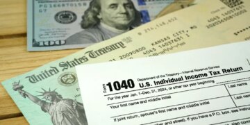 A 1040 tax form, U.S. Treasury check, and $100 bill on a wooden surface.