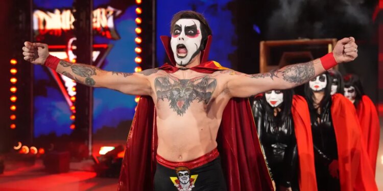 Wrestler Danhausen with painted face and red cape, arms outstretched, with other costumed people behind him.
