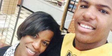 A smiling woman and a young man in a graduation cap and gown with a gold stole featuring a black "M" logo.