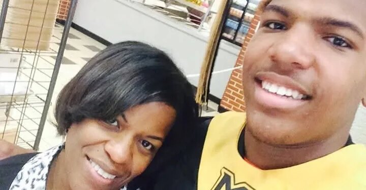 A smiling woman and a young man in a graduation cap and gown with a gold stole featuring a black "M" logo.