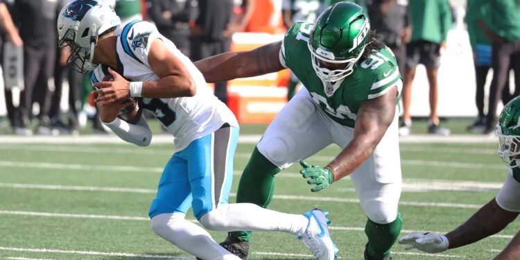Carolina Panthers player Bryce Young running with the ball as New York Jets player Jowon Briggs rushes him.