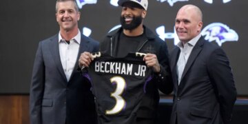 Odell Beckham Jr. holds up a Ravens jersey with head coach John Harbaugh and general manager Eric DeCosta at a news conference.