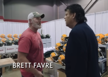 Brett Favre talking to a man in a booth filled with Riddell helmets.