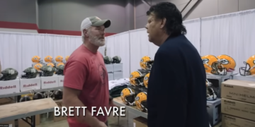 Brett Favre talking to a man in a booth filled with Riddell helmets.