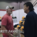 Brett Favre talking to a man in a booth filled with Riddell helmets.