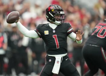 Kyler Murray in a black uniform with a red number 1, throwing a football.