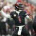 Kyler Murray in a black uniform with a red number 1, throwing a football.
