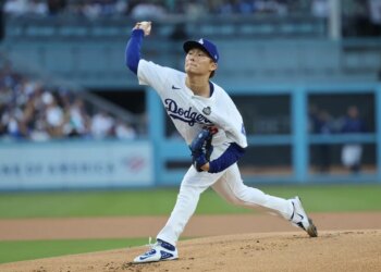 A baseball pitcher in a white uniform with "Dodgers" written across the chest throws a pitch from a mound.