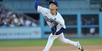 A baseball pitcher in a white uniform with "Dodgers" written across the chest throws a pitch from a mound.