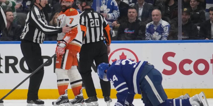 Anaheim Ducks defenseman Radko Gudas (7) looks at injured Toronto Maple Leafs forward Auston Matthews (34) after a knee-on-knee hit, as two referees stand between them.
