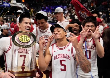 Arkansas players Trevon Brazile, Darius Acuff Jr., and Jaden Karuletwa celebrating their tournament victory with the trophy.