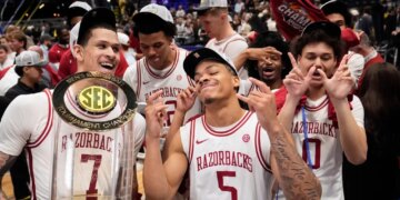 Arkansas players Trevon Brazile, Darius Acuff Jr., and Jaden Karuletwa celebrating their tournament victory with the trophy.