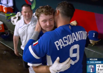 Two baseball players from Team Italy, one wearing number 9, hug while a man in a white polo smiles in the background.