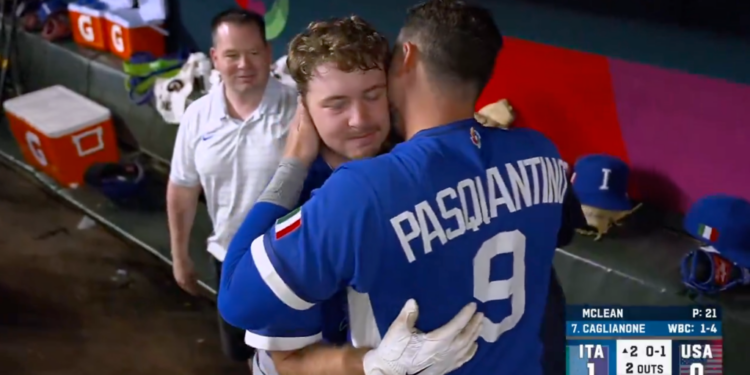 Two baseball players from Team Italy, one wearing number 9, hug while a man in a white polo smiles in the background.