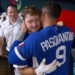 Two baseball players from Team Italy, one wearing number 9, hug while a man in a white polo smiles in the background.