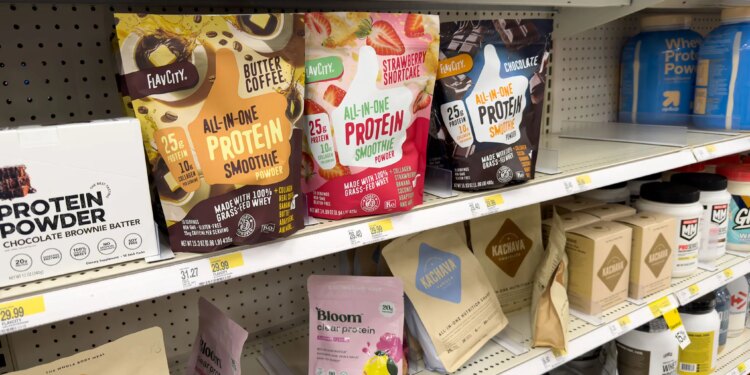 Photo of a protein aisle at Target showing an All-in-one protein smoothie in a butter coffee flavor, as well as strawberry shortcake and chocolate, among several other protein powders.