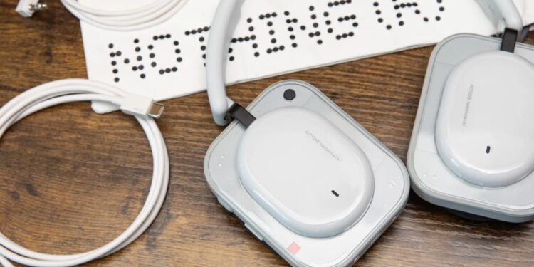 The Nothing Headphone A with its carrying bag, 3.5mm cable, and USB-C cable on a wooden desk with an iPhone nearby.