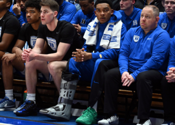 Injured Duke Blue Devils guard Caleb Foster wearing a walking boot on the bench.  Injured Duke Blue Devils guard Caleb Foster (center) looks on with a while wearing a walking boot during the second half against the North Carolina Tar Heels at Cameron Indoor Stadium.