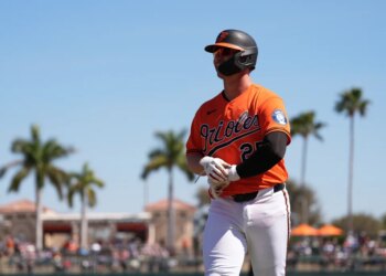 Pete Alonso in an orange Orioles uniform, with a black helmet and sunglasses, walks off the field.