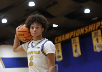 Hofstra basketball player Preston Edmead holding a basketball on his shoulder, with "Championships" banners in the background.