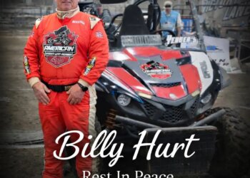 Photo of race official Billy Hurt in a red racing suit standing next to a dirt track racing vehicle.