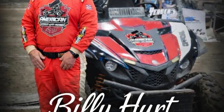Photo of race official Billy Hurt in a red racing suit standing next to a dirt track racing vehicle.
