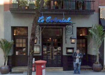 The exterior of the now closed Le Colonial restaurant on East 57th Street in New York, with a neon blue sign and a man looking at his phone.