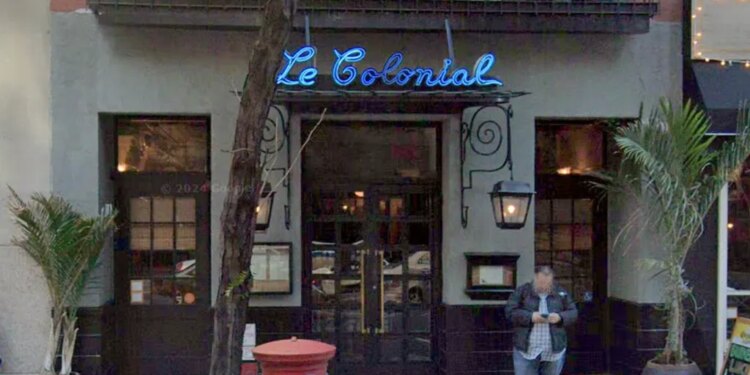 The exterior of the now closed Le Colonial restaurant on East 57th Street in New York, with a neon blue sign and a man looking at his phone.