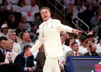 St. John’s head coach Rick Pitino in a white suit, gesturing during a game.