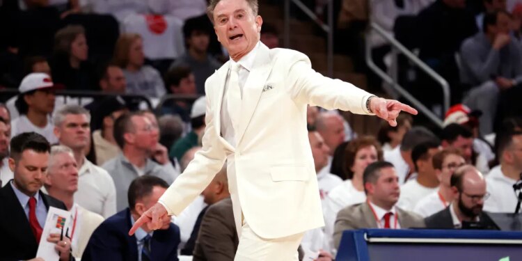 St. John’s head coach Rick Pitino in a white suit, gesturing during a game.