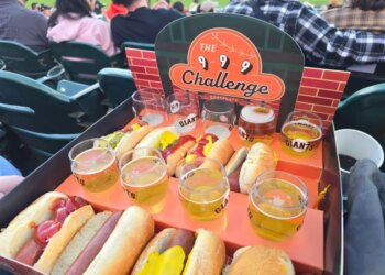 A tray of 9 small beers and 9 hot dogs at a baseball stadium with "The 9-9-9 Challenge" sign.